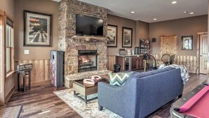 A living room with a stone fireplace, a flat-screen TV, a sofa, and a dining area. - Cabin Unwined (Morganton)