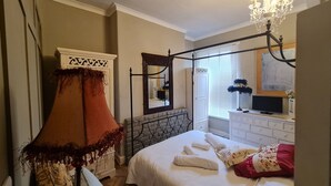 A bedroom with a four-poster bed, a chandelier, a stone fireplace, a television, and a large mirror. - Beautifully Decorated 1-bed Apartment in Sale (Sale)