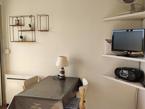 A small, neatly arranged room with a table, chairs, a lamp, a television, and a radio.