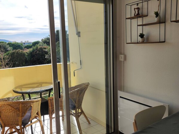 A balcony with wicker chairs, a small table, and a view of greenery and buildings.