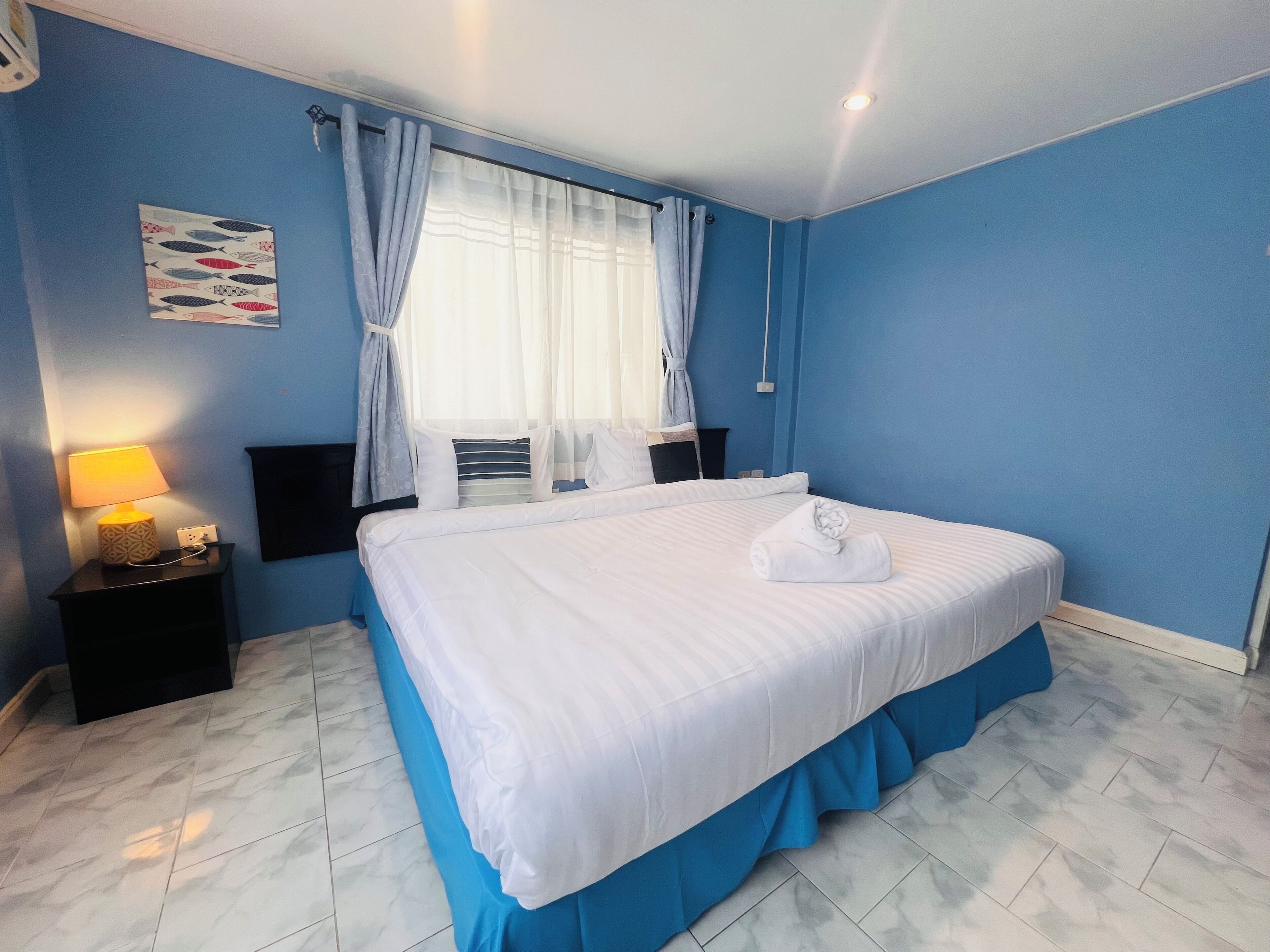 A neatly made bed with a blue skirt, a bedside lamp, and a wall-mounted TV.