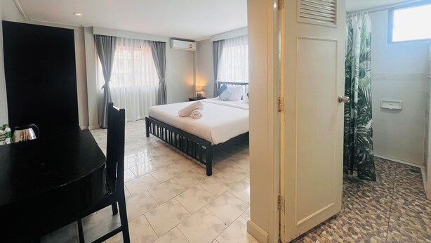 A hotel room with a bed, a desk, and a shower area. - Minotel Patong (Patong)