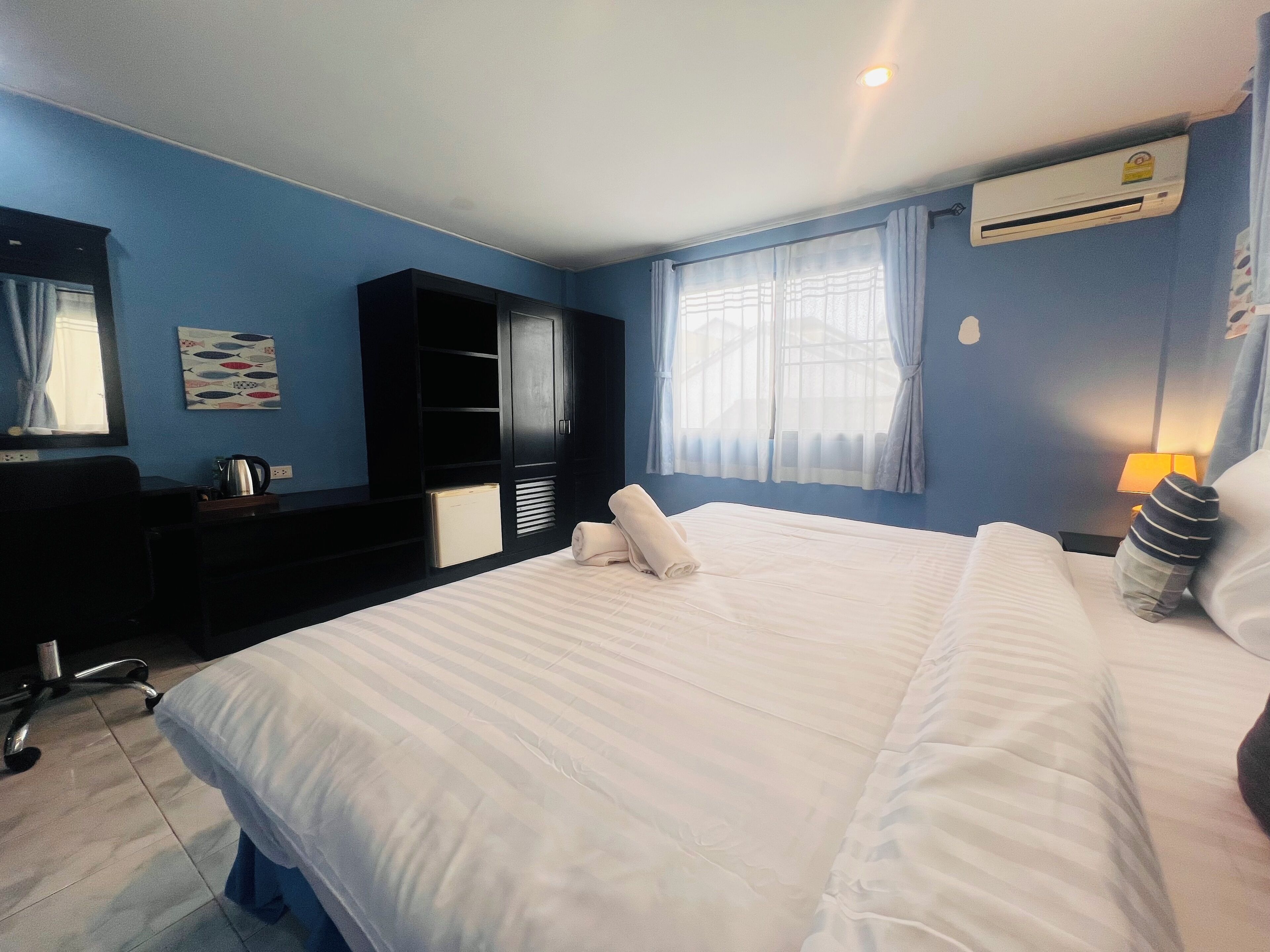 Habitación de hotel con una cama grande, un armario, un escritorio con hervidor y una ventana con cortinas.