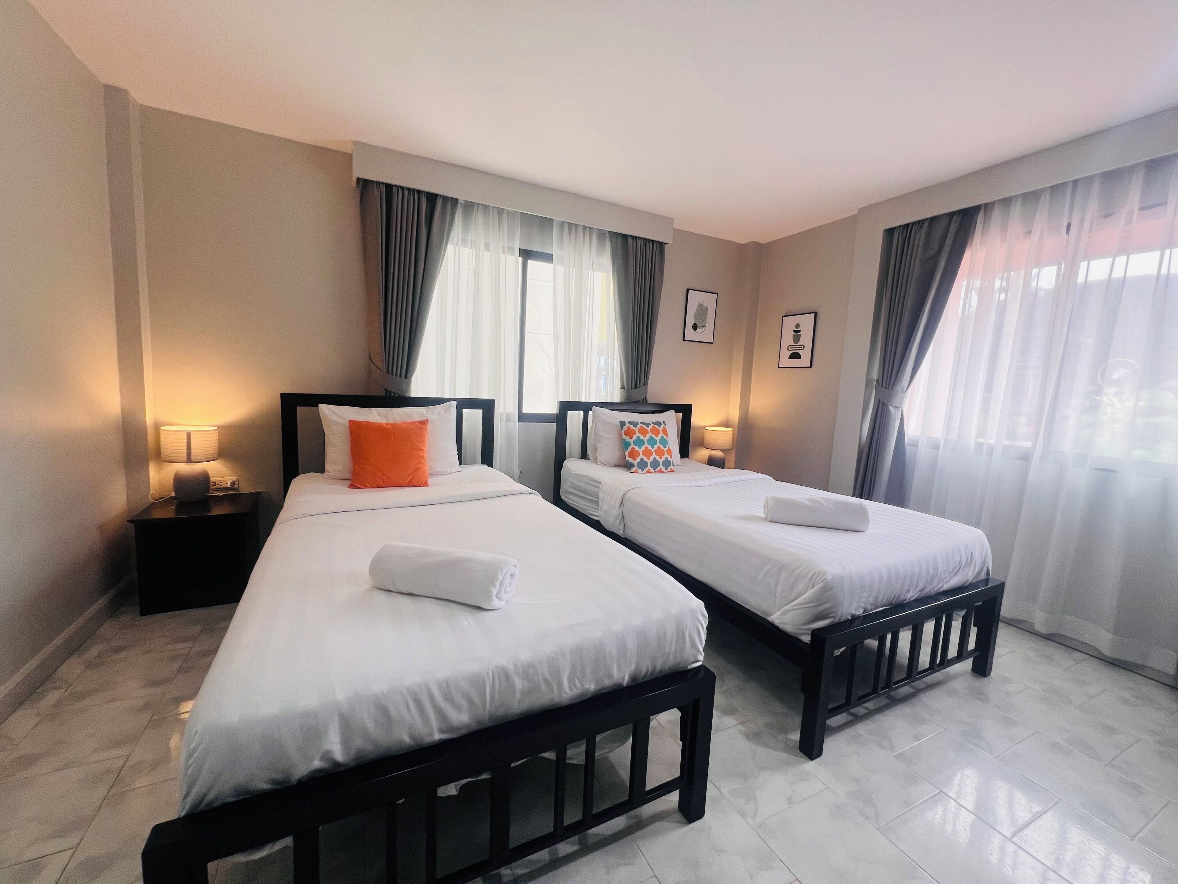 A hotel room with two beds, each with white bedding and a black headboard. There are two bedside tables with lamps, and the room has a tiled floor.