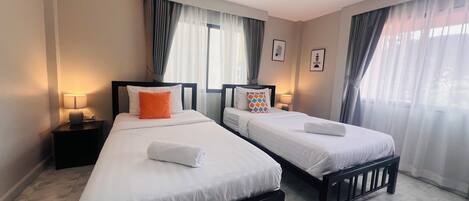 A hotel room with two beds, each with white bedding and a black headboard. There are two bedside tables with lamps, and the room has a tiled floor.
