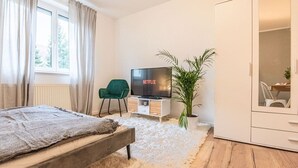 Une chambre à coucher avec un lit, une télévision, un fauteuil vert, une plante en pot et une armoire.