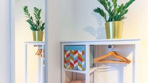 Una habitación con un armario blanco que contiene una planta, una obra de arte con un estampado geométrico colorido y un perchero de madera.
