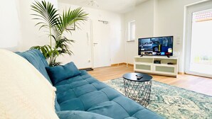Una sala de estar con un sofá azul, un televisor, una planta y una mesita redonda.