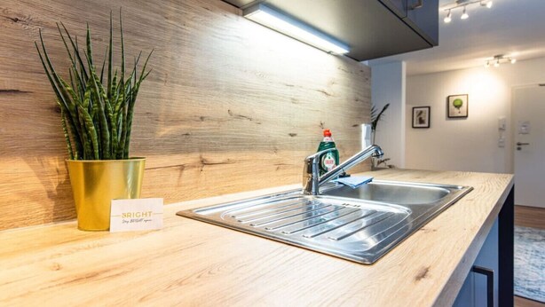 Una cocina con un lavamanos de acero inoxidable, una planta de color dorado y un letrero que dice "BRIGHT Stay BRIGHT".