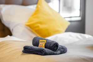 Een netjes opgemaakt bed met een gevouwen handdoek en een kussen.