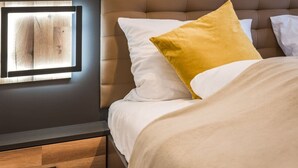 Una cama bien tendida con almohadas blancas y mostaza, un cabecero de madera y una mesita de noche con un cajón.