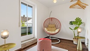 A modern room with a large window, a hanging chair, a small table, and a potted plant.