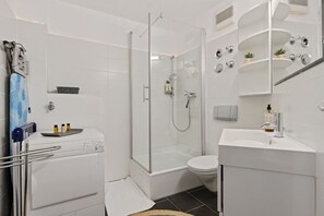 Ein modernes Badezimmer mit einer gläsernen Duschkabine, einem weißen Waschbecken und einer Toilette.