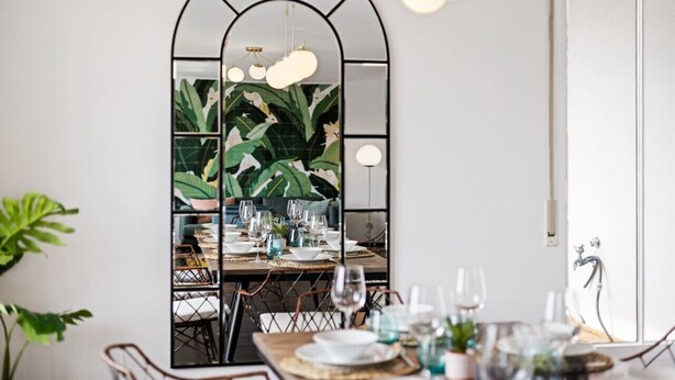 A dining area with a mirrored wall, a wooden table set for four, and a modern chandelier.