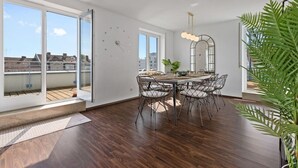 A modern dining area with a wooden table and chairs, large windows, and a view of buildings.