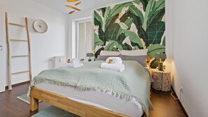 A bedroom with a bed, a ladder, a wall-mounted light fixture, and a large tropical leaf-patterned wall.