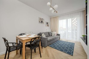 Un salon moderne comprenant une table à manger, un canapé et une grande fenêtre ornée de rideaux légers.