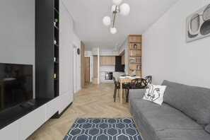 A modern living room with a grey sofa, a dining table, and a kitchen in the background.