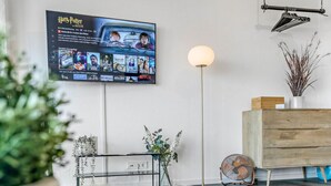 Ett modernt vardagsrum med en platt-TV som visar en film, en golvlampa, ett träskåp och ett glasbord med dekorativa föremål.