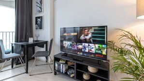 Un soggiorno moderno con una TV a schermo piatto che mostra l'interfaccia di un servizio di streaming, una zona pranzo con tavolo e sedie e una pianta in vaso.