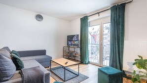 A modern living room with a grey sofa, a wooden coffee table, and a TV stand with a screen.