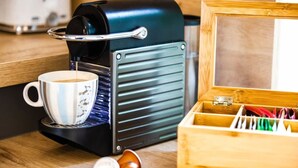 A coffee machine with a cup of coffee, a wooden box, and a metal container on a wooden surface.