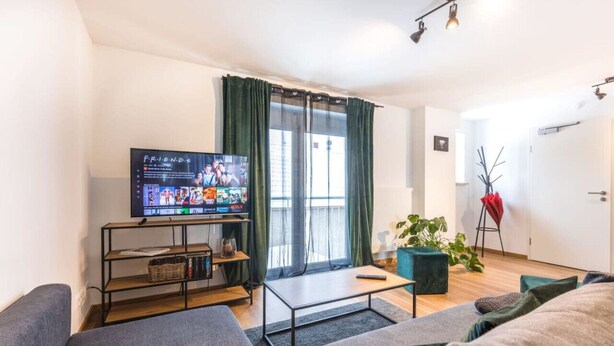 A modern living room with a flat-screen TV on a stand, a sofa, a coffee table, and a potted plant.