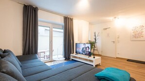 A modern living room with a large sofa, a flat-screen TV, and a balcony with a sliding door. - Arbio I Beach style Apart (Augsburg)