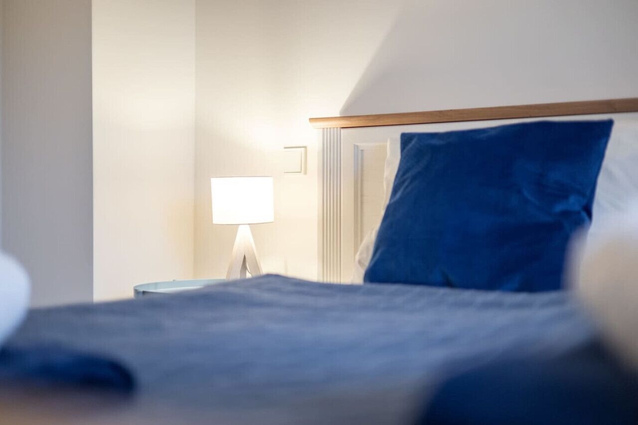 Una camera d'albergo con un letto, un comodino e una lampada.
