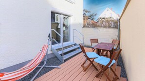 A patio with a wooden table and chairs, a striped hammock, and a glass door leading to a staircase. - Arbio I Beach style Apart (Augsburg)