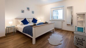 A bedroom with a bed, bedside tables, a window, a radiator, a mirror, and a storage unit. - Arbio I Beach style Apart (Augsburg)