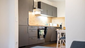 A compact kitchen with grey cabinets, a built-in oven, and a wooden backsplash. - Arbio I Beach style Apart (Augsburg)