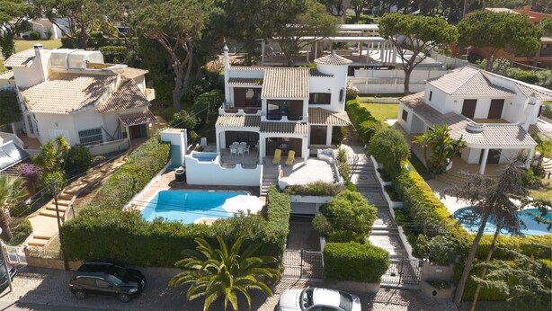 Uma casa de vários andares com piscina, um carro estacionado em frente e um jardim bem cuidado.