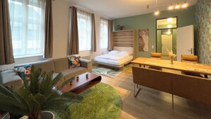 Quarto de hotel moderno com cama, sofá, mesa de jantar e uma planta verde.