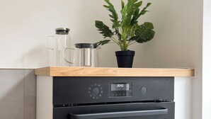 Cozinha compacta com forno embutido, cafeteira e planta em vaso sobre a bancada.