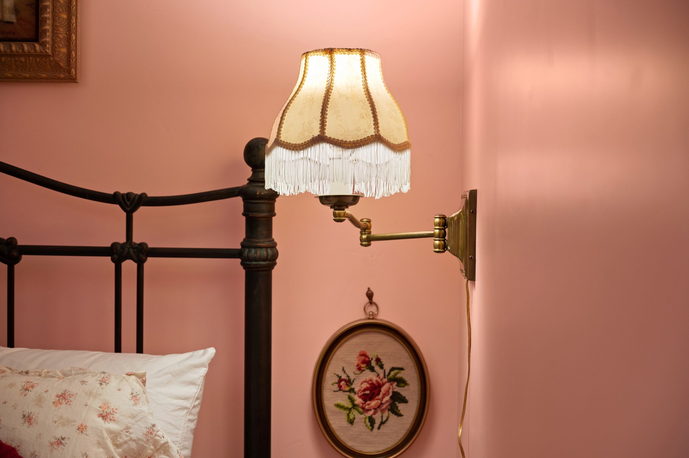 A bed with a headboard, a wall-mounted lamp, and a framed floral artwork.