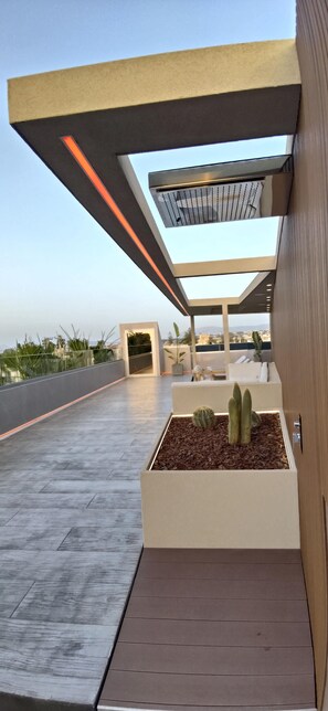 A modern outdoor area with a wooden deck, a planter with cacti, and a glass ceiling structure. - Summertime Signature Suites (Chania)