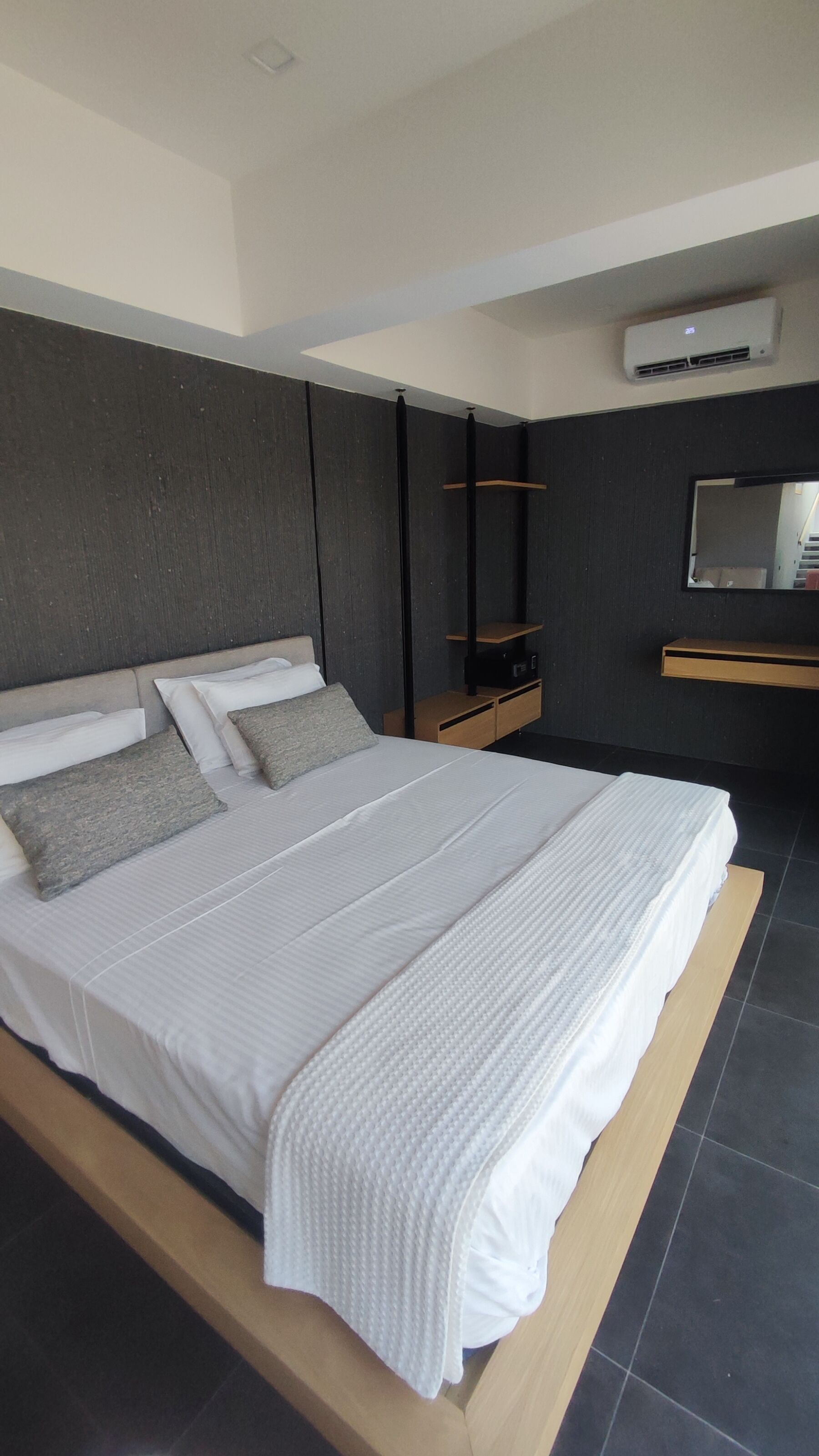 A modern bedroom with a large bed, a bedside table, a small cabinet, and a wall-mounted air conditioning unit.