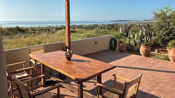 Une table et des chaises en bois, placées sous une pergola, offrent une vue sur la mer et le paysage environnant.
