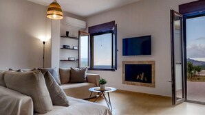 Un salon moderne avec un canapé, une petite table ronde agrémentée d’une plante, une cheminée et un téléviseur fixé au mur.