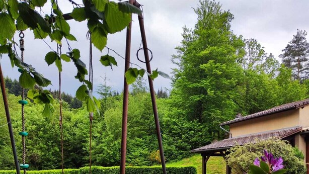 A garden with a swing set, a well-maintained lawn, and a building with a tiled roof. - Country house in Livradois Forez (Saint-Victor-Montvianeix)