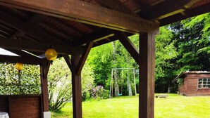 A covered patio area with a table and chairs, surrounded by a stone floor and a grassy lawn. - Country house in Livradois Forez (Saint-Victor-Montvianeix)