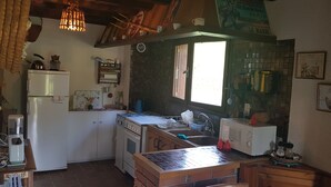 A compact kitchen with a refrigerator, stove, microwave, and sink. There is a window providing natural light, and various kitchen items are visible. - Country house in Livradois Forez (Saint-Victor-Montvianeix)