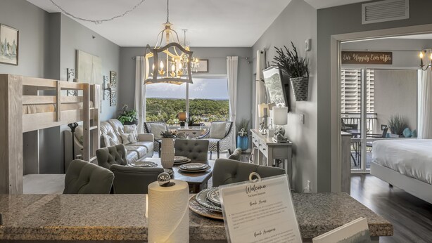 A modern hotel room with a dining area, a large window with a view, and a sign welcoming guests. - Luau *5th Floor* Condo, 1 bedroom plus bunk beds at Sandestin Golf & Beach Resort! (Miramar Beach)