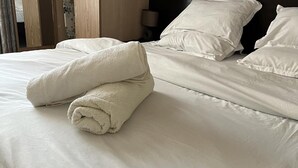 Un lit bien fait, avec des draps blancs et une serviette blanche enroulée posée sur le dessus.