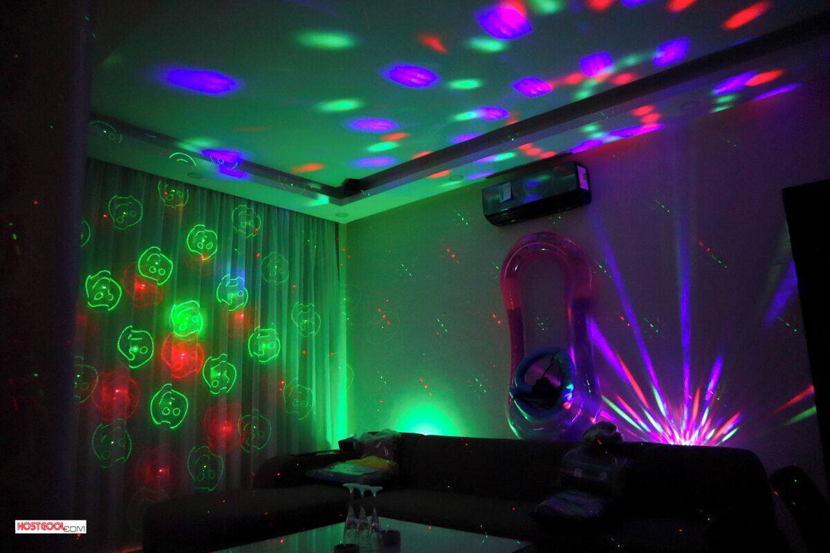 A room with a ceiling projector displaying colorful patterns, a couch, and a wall-mounted projector.