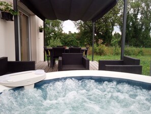 A hot tub with a wooden deck, outdoor furniture, and a table with chairs. - Maison Avec Spa Privé (Saint-Gervais)