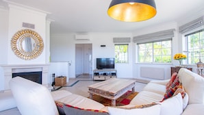 A living room with a sofa, television, fireplace, and large windows. - 42 Presa do Moura, beautiful townhouse on stunning complex with pool and gym! (Carvoeiro)