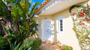 A house with a white door, a cobblestone pathway, and lush tropical plants. - 42 Presa do Moura, beautiful townhouse on stunning complex with pool and gym! (Carvoeiro)
