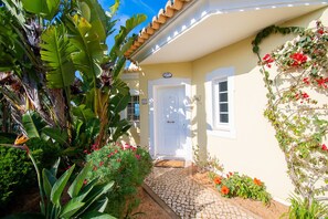 A house with a white door, a cobblestone pathway, and lush tropical plants.